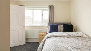 Une chambre à coucher avec un lit, une table de chevet, une fenêtre avec des rideaux et un radiateur.