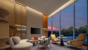 Uma sala de estar moderna com televisão de tela plana, assentos confortáveis, uma mesa de centro e grandes janelas com vista para o céu e árvores.