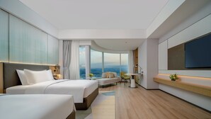 Quarto de hotel com duas camas, um sofá, uma televisão e vista para a cidade.