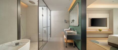 A modern bathroom with a glass shower enclosure, a bathtub, a vanity with a mirror, and a bed in the adjacent room.