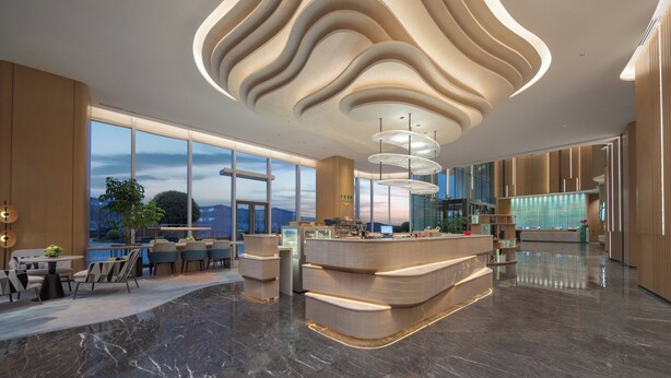 Um lobby de hotel moderno com teto curvo, balcão de recepção e vista para a paisagem urbana.