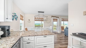 A kitchen with a granite countertop, white cabinetry, and a view of the ocean through large windows. - Oceanfront Updated 5BR Duplex. Dog friendly! (Emerald Isle)