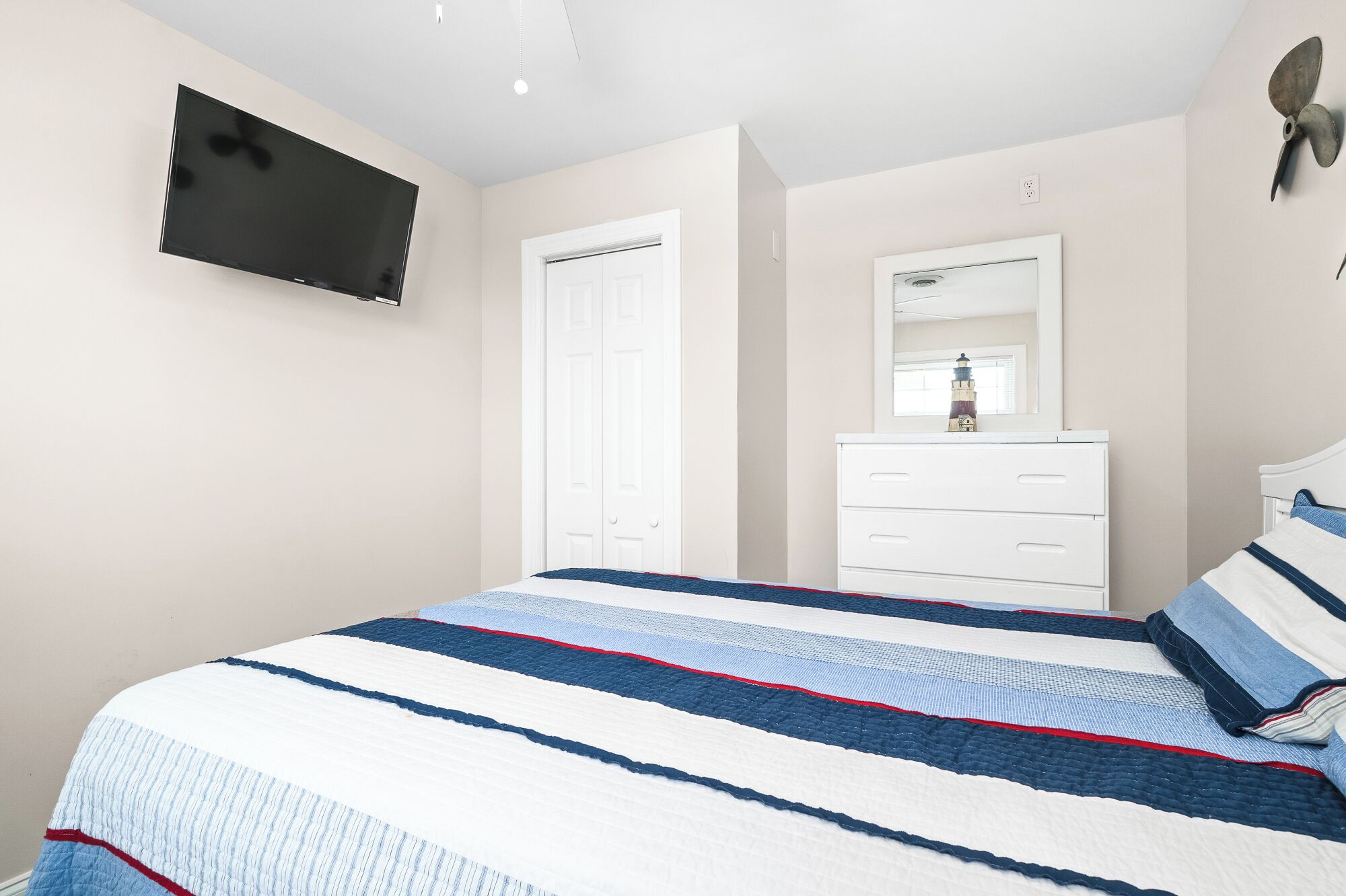 A bedroom with a bed, a dresser, a mirror, and a television on the wall.