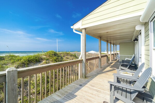 A wooden deck with chairs, overlooking a beach and ocean.