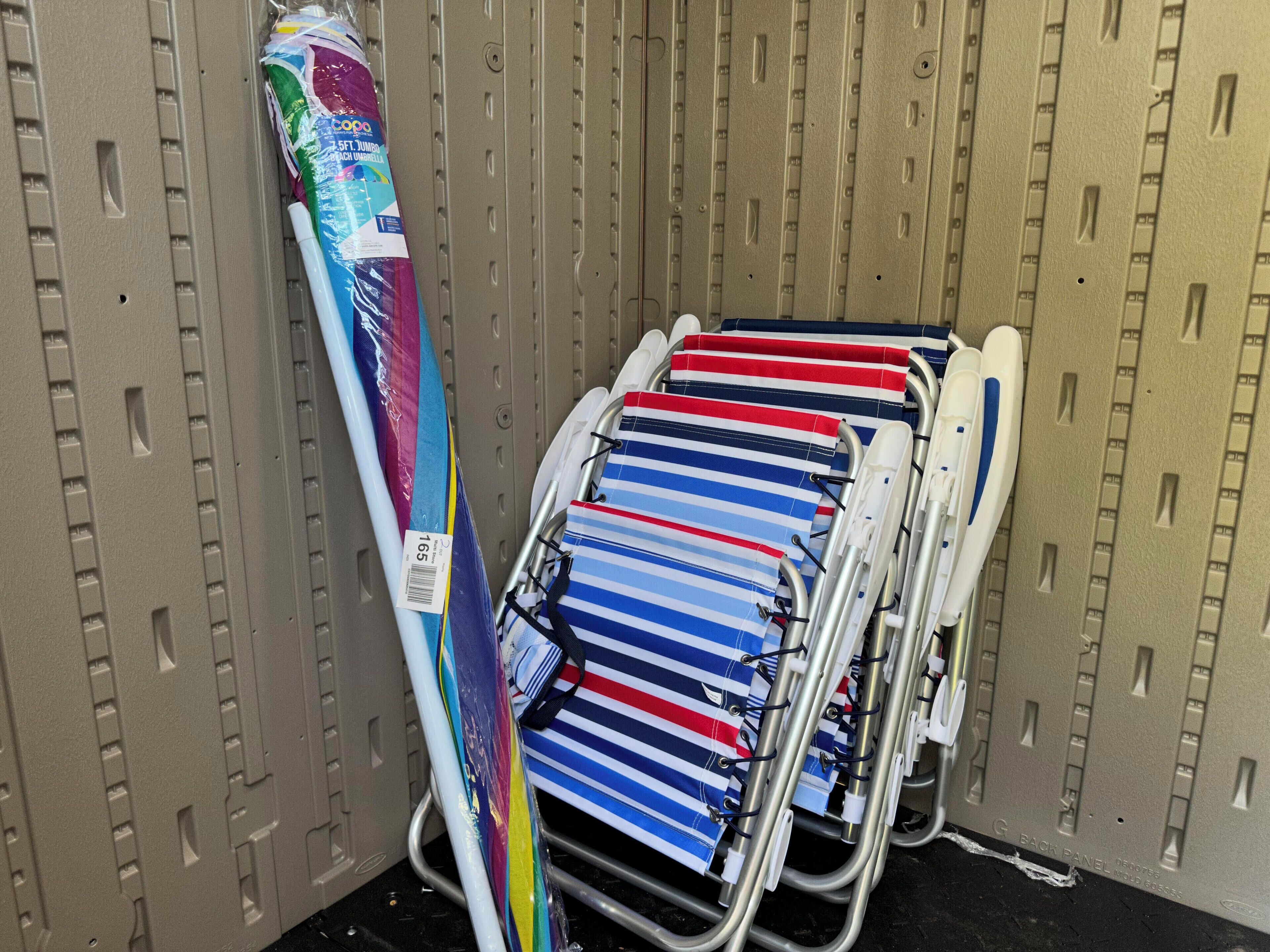 A metal cart with striped umbrellas and a beach umbrella in a storage area.