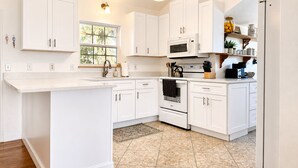 A kitchen with white cabinets, a central island, a microwave, an oven, and a sink. - 1 Minute Walk to Ocean-Charming Downtown Beachside Home with Mother-In-Law Suite (Cocoa Beach)