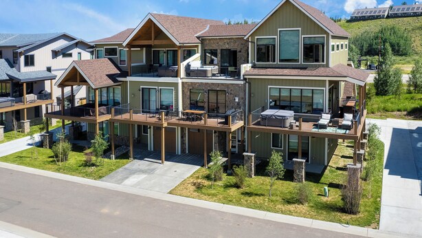 A modern multi-story residential building with a spacious deck area, large windows, and a hillside backdrop. - Mountain Getaway | Hot Tub & Year-Round Fun (Fraser)