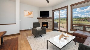 A modern living room with a fireplace, a television, and a large window offering a scenic view. - Mountain Getaway | Hot Tub & Year-Round Fun (Fraser)
