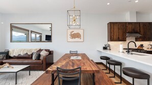 A modern kitchen with wooden cabinets, a dining table with benches, and a large window overlooking a mountainous landscape. - Mountain Getaway | Hot Tub & Year-Round Fun (Fraser)