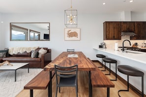 Una cocina moderna con armarios de madera, una mesa de comedor con bancos y un ventanal con vistas a un paisaje montañoso.