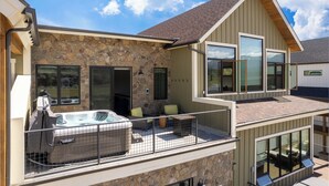 A modern house with a stone facade, a hot tub, and a balcony with outdoor seating. - Mountain Getaway | Hot Tub & Year-Round Fun (Fraser)