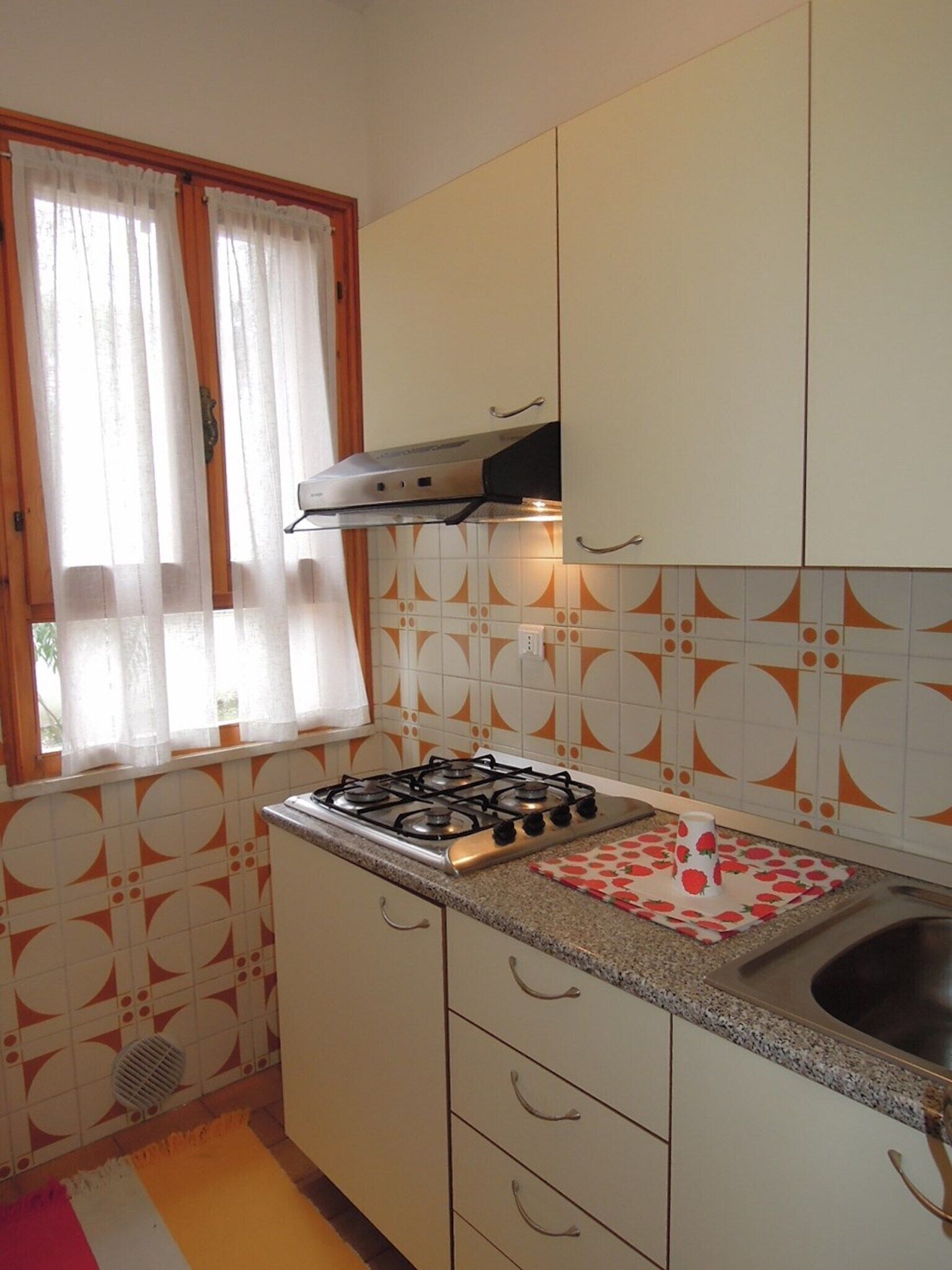 A kitchen with a gas stove, a sink, and a window with curtains.