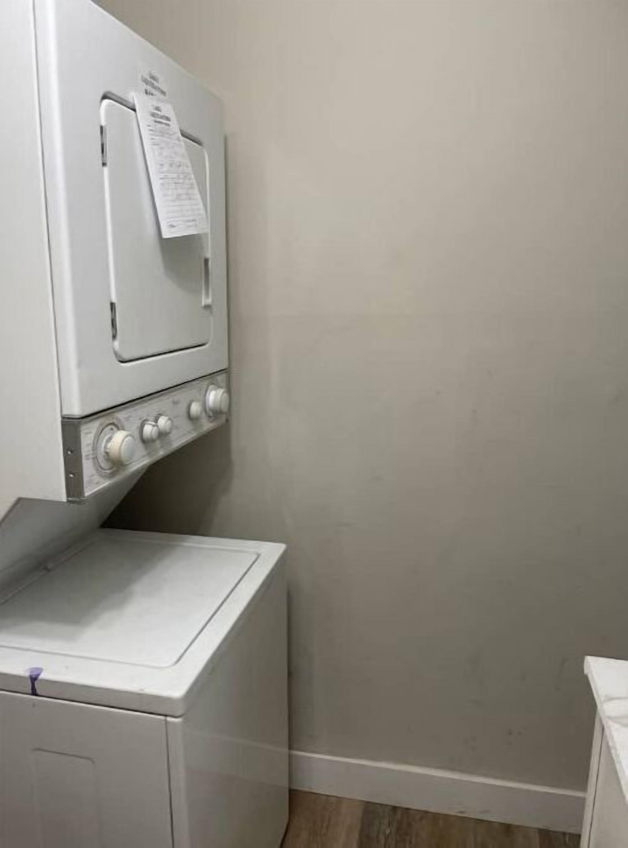 A laundry room with a front-loading washer and dryer, a wall-mounted paper towel dispenser, and a small shelf.
