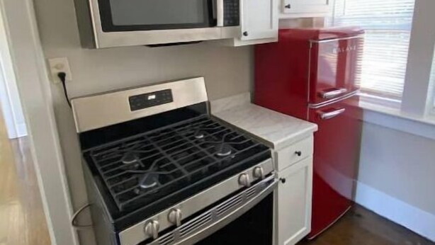 Cocina compacta con armarios blancos, estufa de acero inoxidable, refrigerador rojo y microondas.