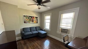 Una habitación con un sofá modular, un ventilador de techo y un cuadro en la pared.