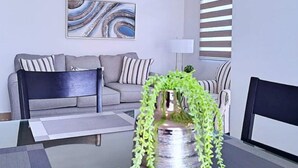 A modern living room with a grey sofa, striped cushions, a black chair, a glass coffee table, and a decorative vase with green plants. - My Escape Dreamy Luxury Home in Bayamón, P.R. (DAVILA BAYAMON PR)