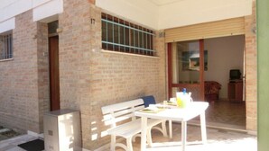 Un pati amb taula i banc blanca, un frigorífic petit i una porta corredissa de vidre que dona a una habitació interior.