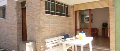A patio with a white table and bench, a small refrigerator, and a sliding glass door leading to an interior room.