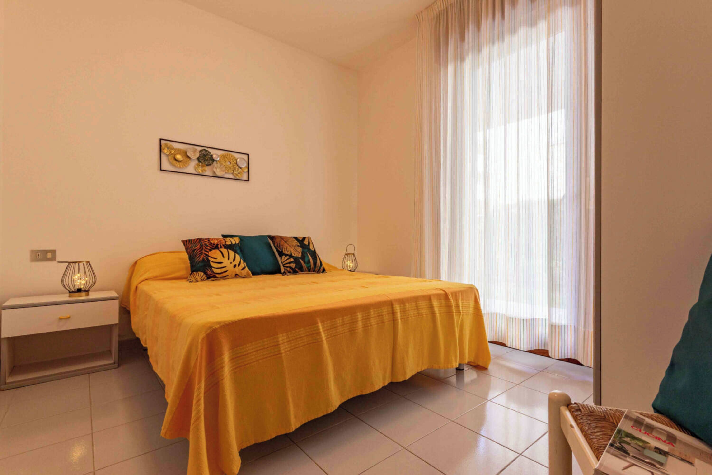 A hotel room with a bed, a nightstand, a lamp, a window with curtains, and a wall-mounted picture.