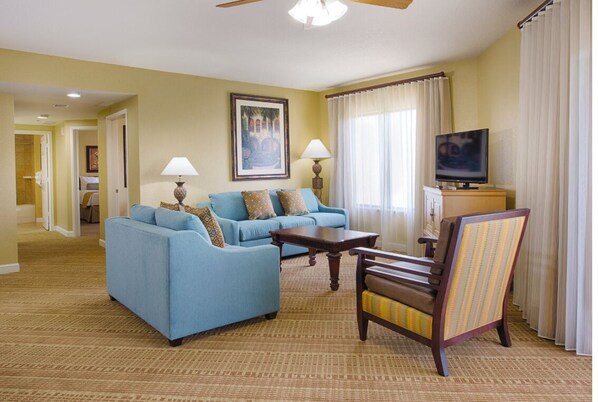 A living room with a blue sofa, a wooden chair, a television, and a painting on the wall.