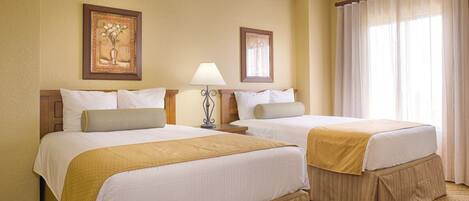 A hotel room with two beds, a nightstand with a lamp, a framed picture on the wall, and a window with curtains.