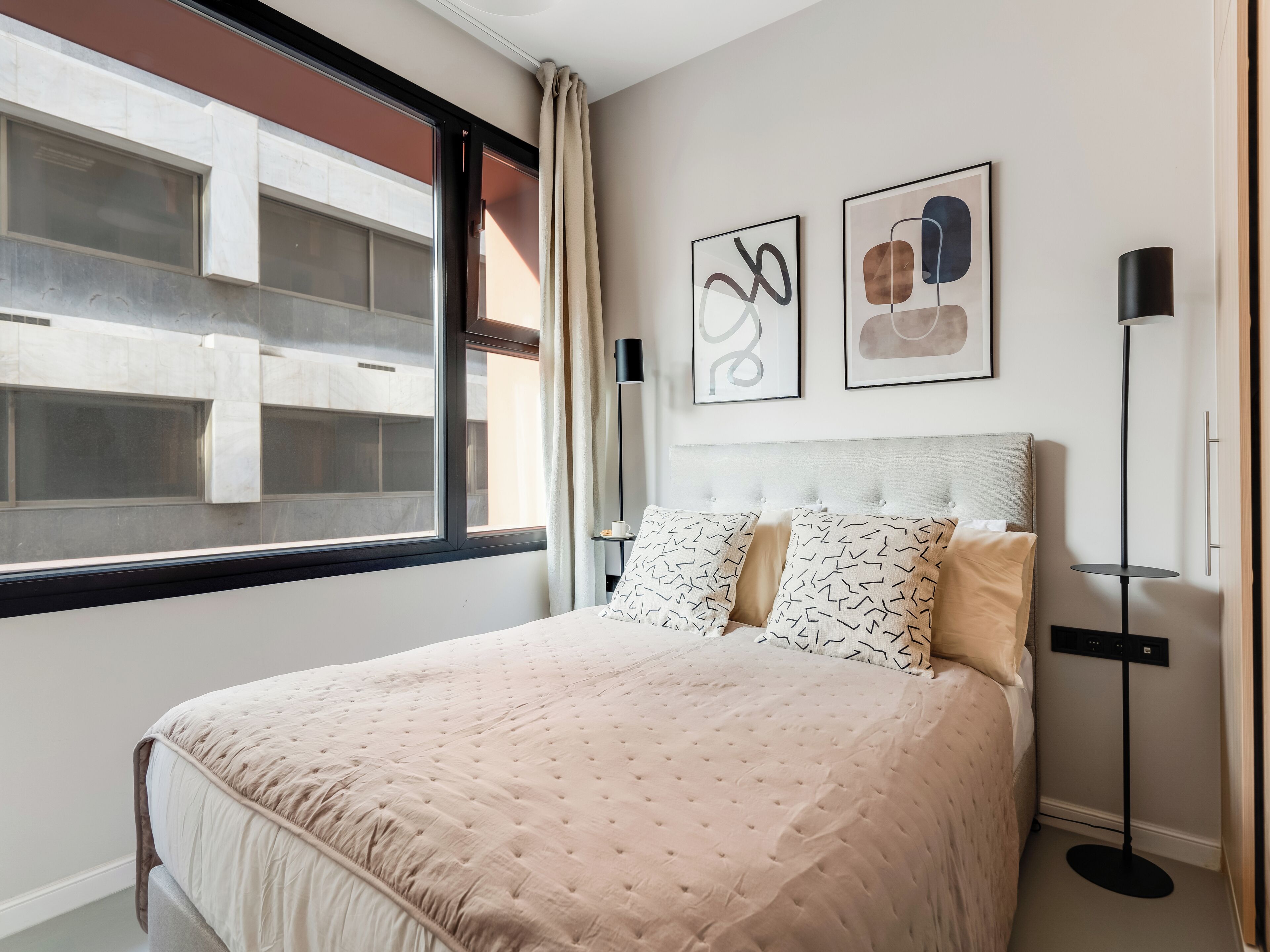A neatly arranged bedroom with a large bed, a floor lamp, and two wall art pieces.