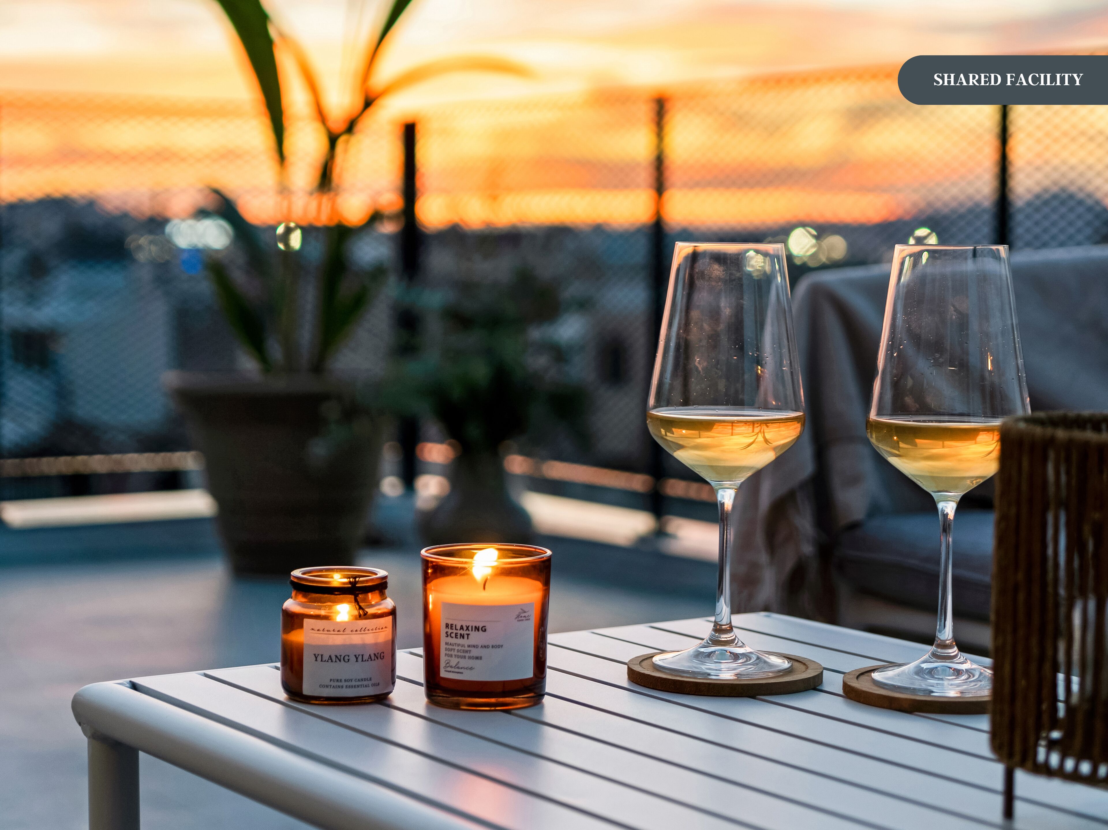 Mesa com duas velas e dois copos de vinho branco numa varanda com vista para o pôr do sol.