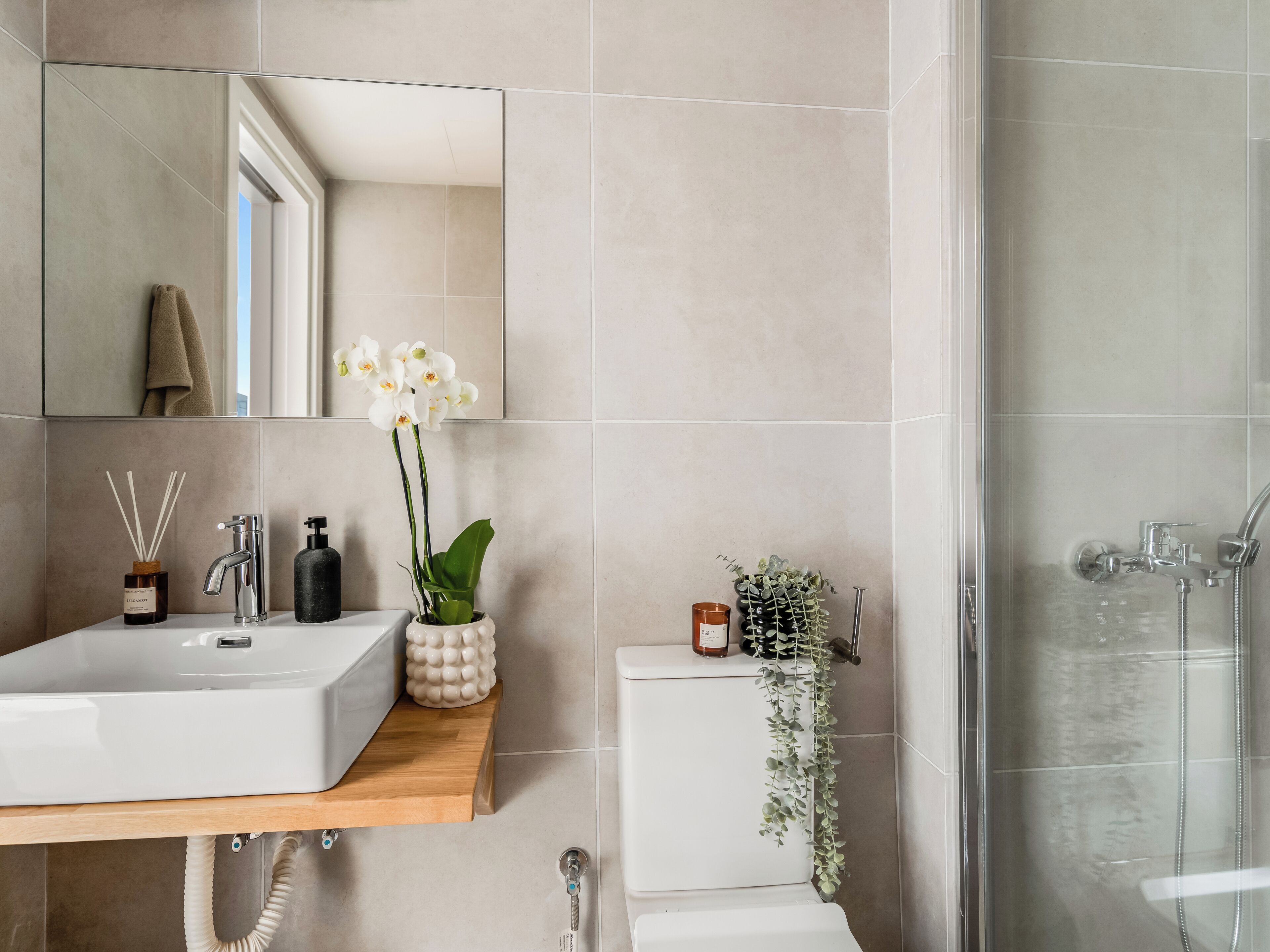Et moderne badeværelse med et stort spejl, en hvid vask, en bruseniche og et toilet.