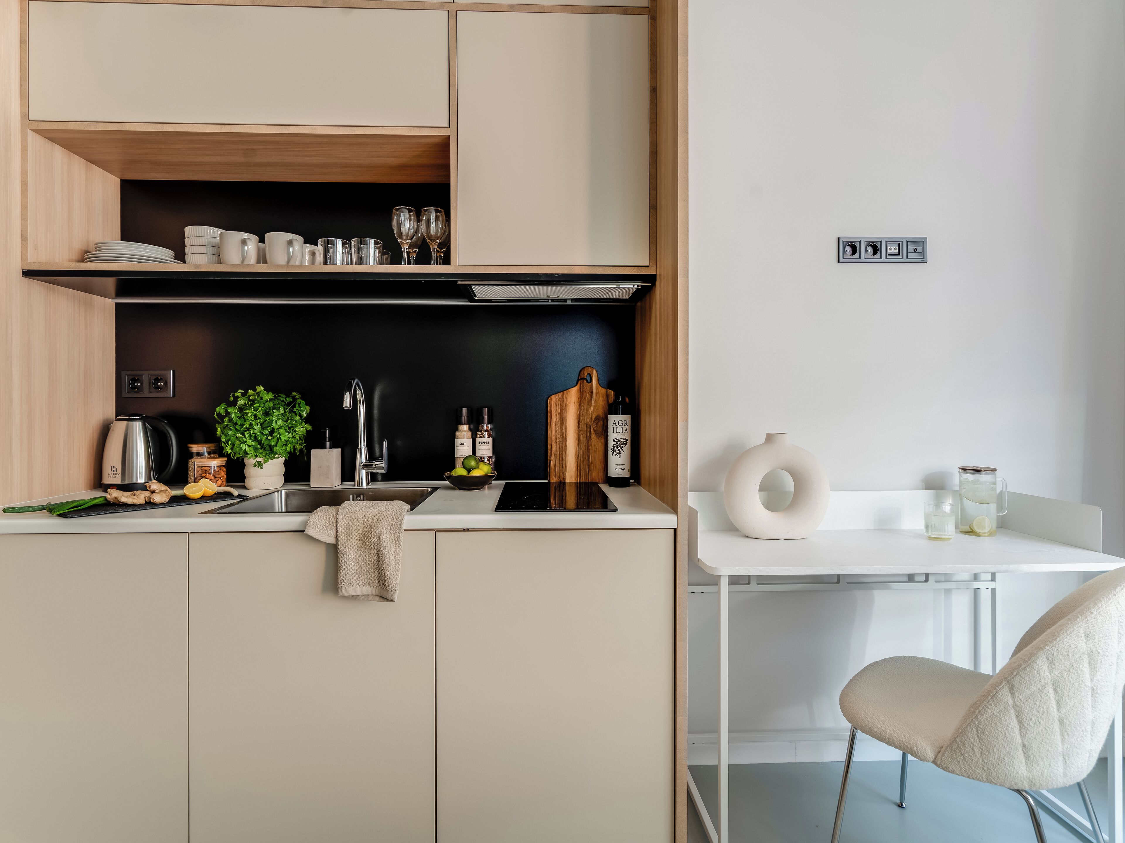 A modern kitchen with a white countertop, a sink, and a dining area with a chair.