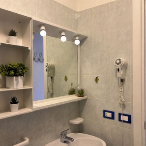 Ein Badezimmer mit einem weißen Waschbecken, einem Spiegel und einem an der Wand befestigten Föhn.