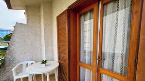 A balcony with a white plastic chair and table, a wooden door with glass panels, and a textured wall.