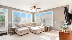 A spacious living room with a large sectional sofa, a ceiling fan, and large windows. - Stay and Play Retreat - Family Home and Game Room (Bellevue)