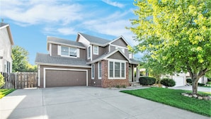 A two-story house with a garage, a well-maintained lawn, and a tree in the front yard. - Stay and Play Retreat - Family Home and Game Room (Bellevue)