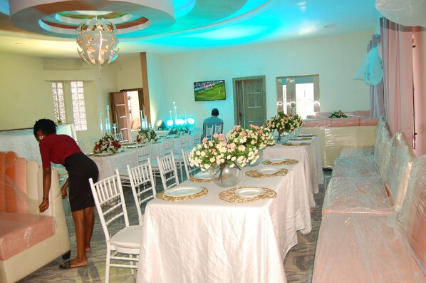 A banquet hall with white tables, chairs, and a large floral centerpiece.