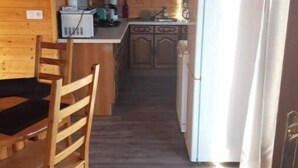 A wooden cabin interior with a dining area, kitchen, and a refrigerator. - Chalet en Bois à la Campagne (Cayres)