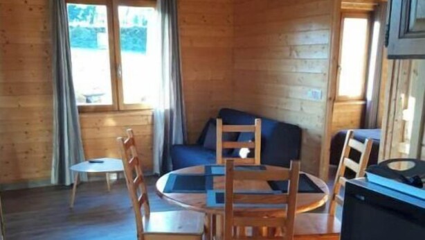 A wooden cabin interior with a round dining table, chairs, a sofa, and a television. - Chalet en Bois à la Campagne (Cayres)
