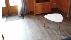 A wooden-paneled room with a television on a wooden stand, a small white table, and a door with curtains. - Chalet en Bois à la Campagne (Cayres)