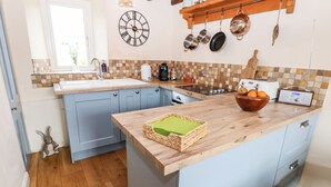 Una cocina con armarios azules, una encimera de madera, un reloj, ollas colgadas y un radio.