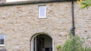 Un edificio de piedra con un arco de entrada que da a un espacio interior. Hay plantas en macetas afuera y una pequeña ventana a la izquierda.