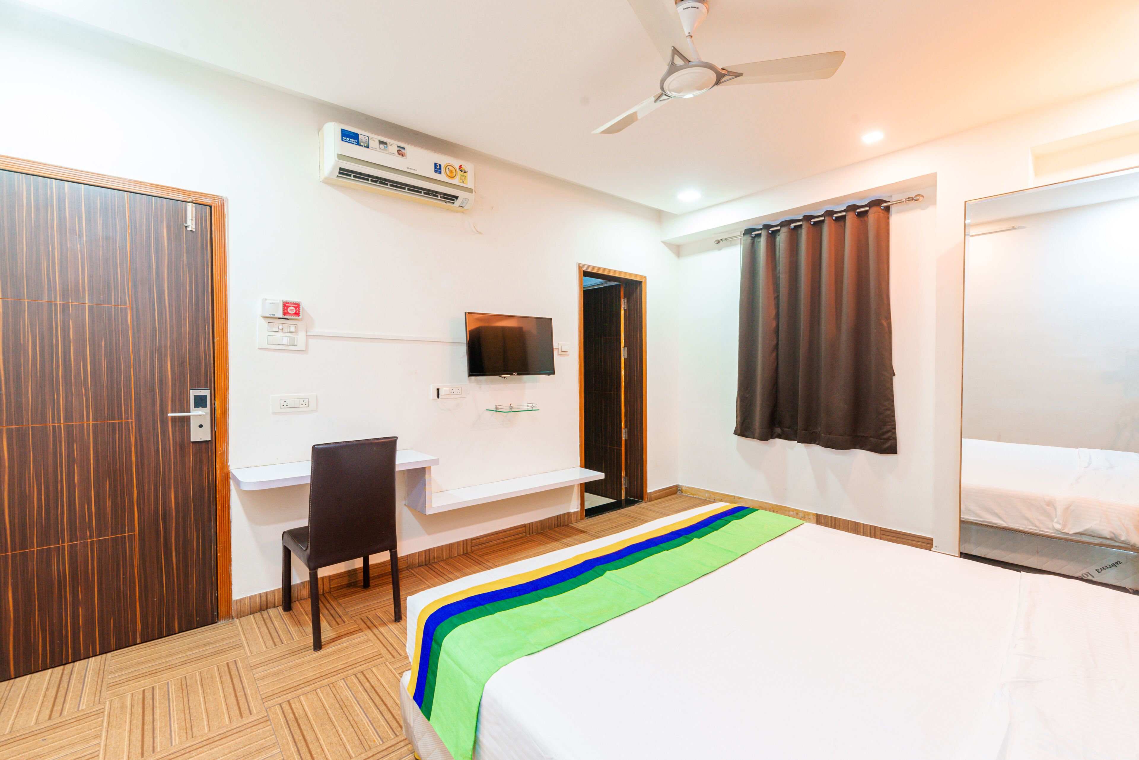 Una habitación de hotel con cama, escritorio, silla, televisor y ventilador de techo.
