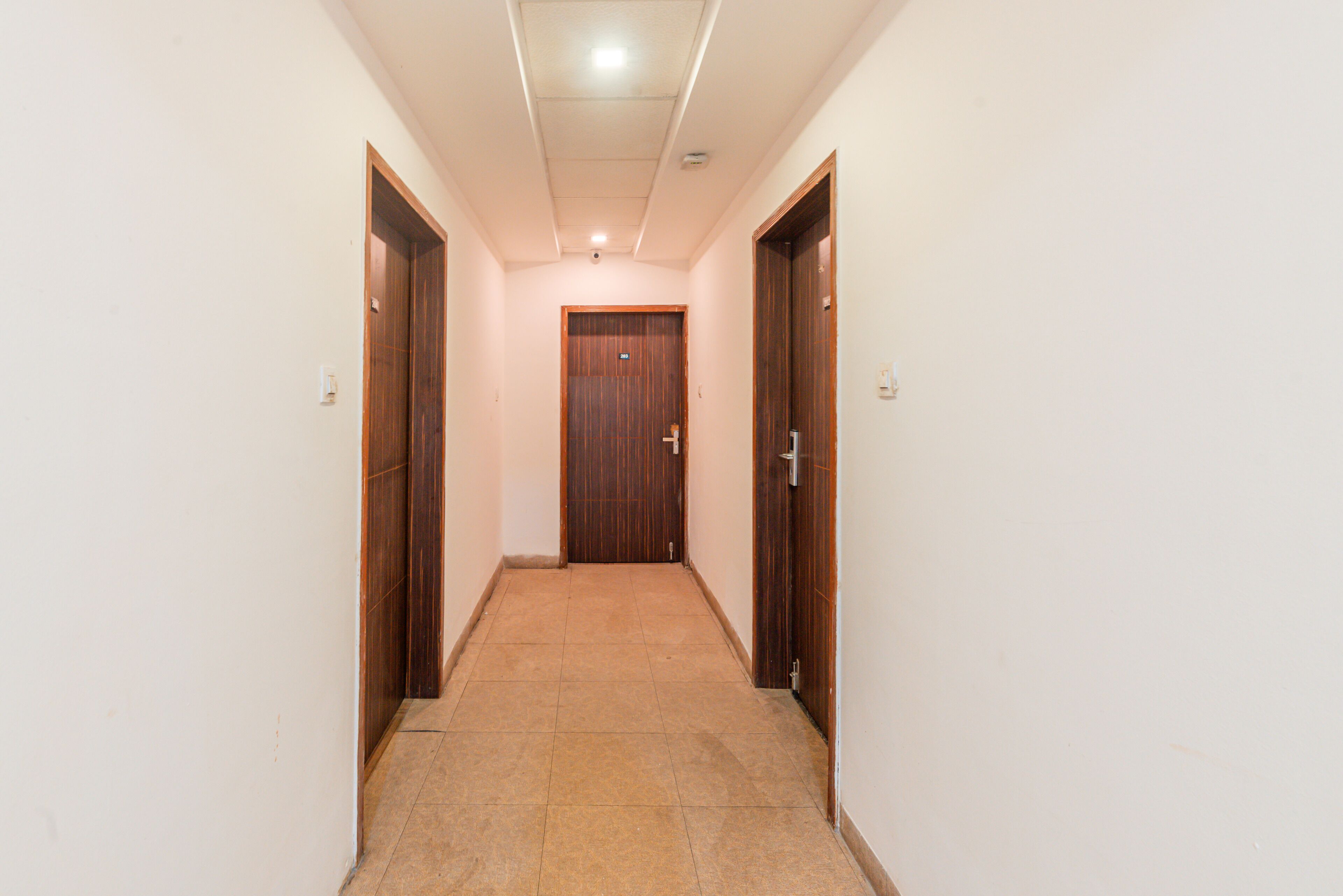 A hallway with wooden doors on either side, a tiled floor, and a ceiling light.