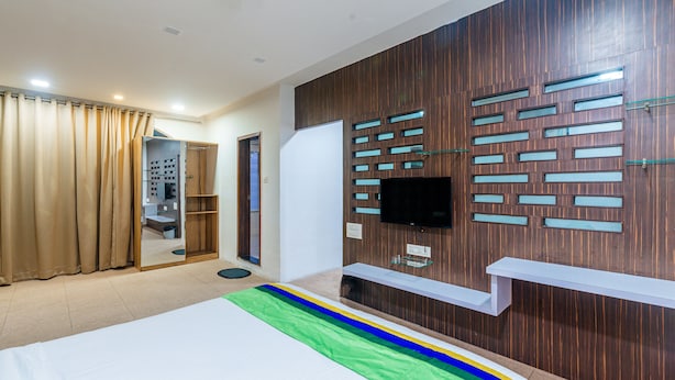Una habitación de hotel moderna con una cama grande, un televisor montado en una pared de madera y un baño visible a través de una puerta abierta.
