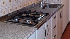 A kitchen with white cabinets, a gas stove, a stainless steel sink, and patterned backsplash tiles. - Nice Three-bedroom Flat With Balcony in Bibione (San Michele al Tagliamento)