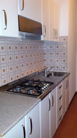 A kitchen with white cabinets, a gas stove, a stainless steel sink, and patterned backsplash tiles. - Nice Three-bedroom Flat With Balcony in Bibione (San Michele al Tagliamento)