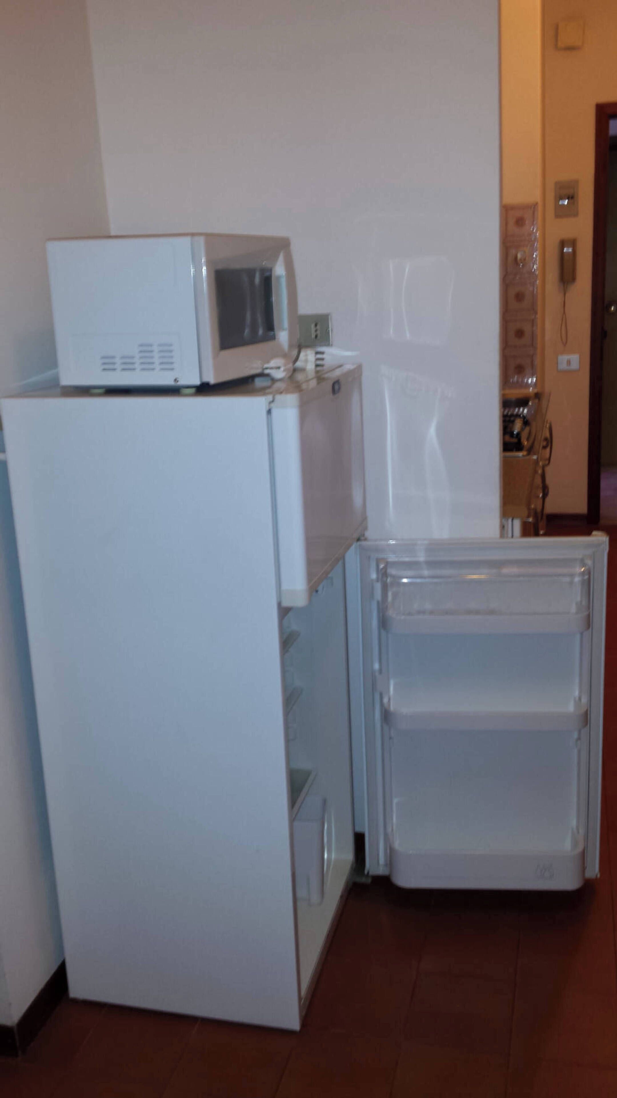 A compact kitchen with a white refrigerator, a microwave on top, and a small refrigerator with a transparent door.