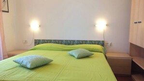 A single-bed room with a green bedspread, two pillows, and two wall-mounted lights. - Nice Three-bedroom Flat With Balcony in Bibione (San Michele al Tagliamento)