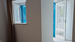 A hotel room with a bed, a nightstand, a window with blue shutters, and a door leading to a balcony. - Double Room, air Conditioning, Bathroom, (Tropea)