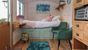 A cozy bedroom with a bed, a green chair, a wooden cabinet, and a painting on the wall. - Lottie's Hut (Okehampton)