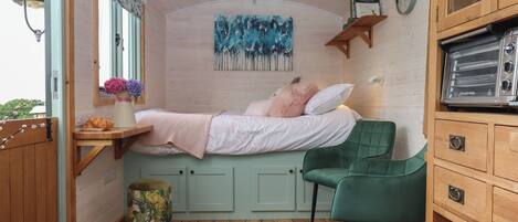 A cozy bedroom with a bed, a green chair, a wooden cabinet, and a painting on the wall.