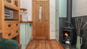 A cozy room with wooden cabinets, a green sofa, a wooden door, and a fireplace with a lantern. - Lottie's Hut (Okehampton)